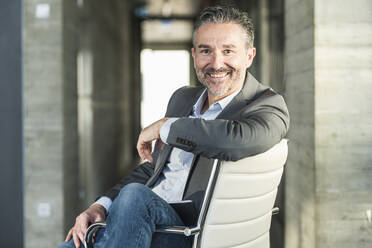 Portrait of a smiling mature businessman sitting on chair in office - UUF20043