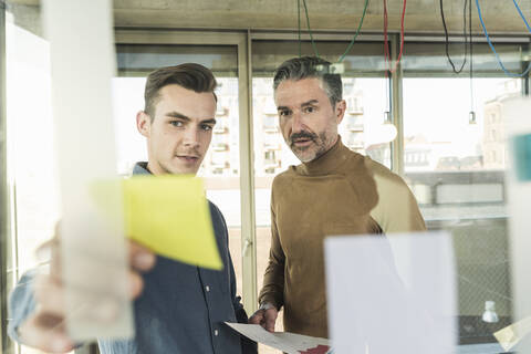 Mature businessman and young man working on adhesive notes at glass pane in office stock photo