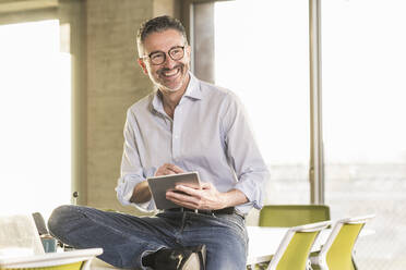 Happy mature businessman with tablet in office - UUF20060