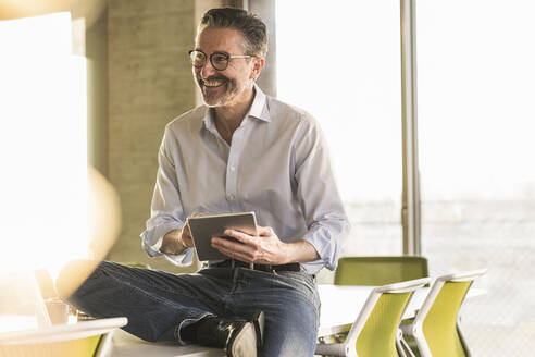 Glücklicher reifer Geschäftsmann mit Tablet im Büro - UUF20061