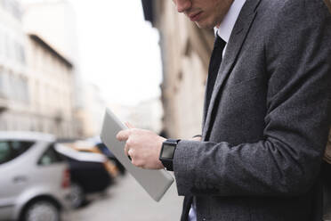 Crop-Ansicht eines jungen Geschäftsmannes mit digitalem Tablet und Blick auf eine Smartwatch - FMOF00852