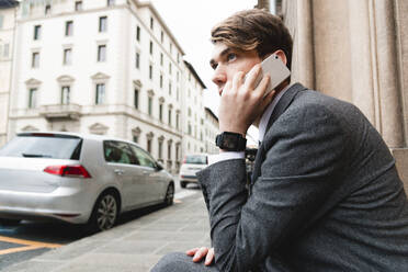 Junger Geschäftsmann mit Smartwatch beim Telefonieren in der Stadt - FMOF00855