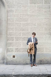 Young businessman standing on pavement looking at smartphone - FMOF00857