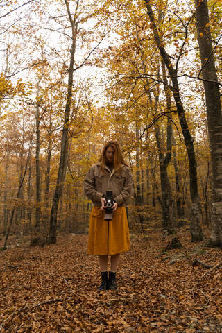 Rothaarige junge Frau fotografiert mit Analogkamera im herbstlichen Wald, lizenzfreies Stockfoto