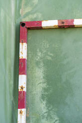 Rusty soccer goal leaning on green wall, partial view - AFVF04920