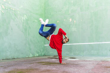 Porträt eines bärtigen jungen Mannes mit rotem Sweatshirt, der einen Handstand auf einer Hand macht - AFVF04927