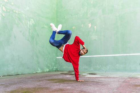 Portrait of bearded young man wearing red sweatshirt doung handstand on one hand - AFVF04927