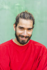 Porträt eines bärtigen jungen Mannes mit gefärbtem Haar und rotem Sweatshirt - AFVF04930