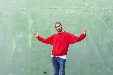 Portrait of angry young man wearing red sweatshirt in front of green wall - AFVF04931