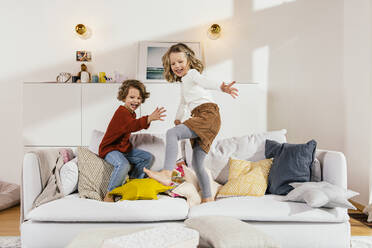 Zwei glückliche Mädchen springen zu Hause auf der Couch herum - MFF04964