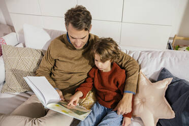 Father reading book with daughter on couch - MFF04972