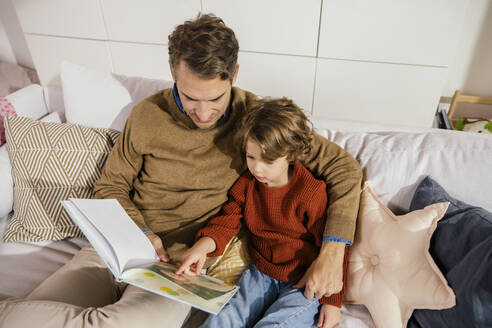 Vater liest mit Tochter auf der Couch ein Buch - MFF04972