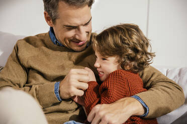 Father playfighting with daughter on couch - MFF04974