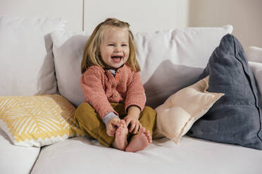 Lachendes kleines Mädchen, das zu Hause auf der Couch sitzt - MFF04977