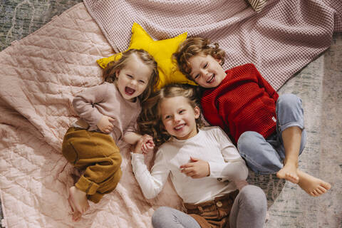 Drei glückliche Mädchen liegen zu Hause auf Decken, lizenzfreies Stockfoto