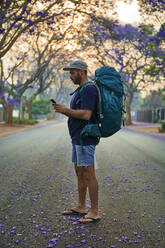 Backpacker using smartphone standing on a street, Pretoria, South Africa - VEGF01264