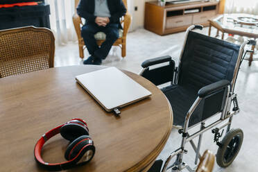 Kopfhörer und Laptop mit USB-Stick auf dem Tisch im Wohnzimmer eines älteren Mannes - JRFF03933