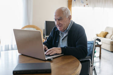 Porträt eines zufriedenen älteren Mannes im Rollstuhl, der zu Hause einen Laptop benutzt - JRFF03935