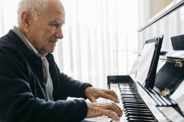 Senior man sitting in wheelchair playing piano at home - JRFF03962