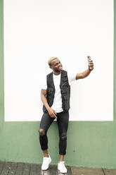 Mann benutzt Smartphone und macht ein Selfie vor einer grün-weißen Wand - OCMF00978