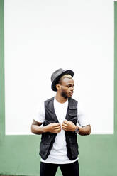 Man wearing hat and looking sideways in front of a green and white wall - OCMF00979