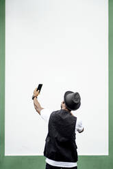 Mann benutzt Smartphone und macht ein Selfie vor einer grün-weißen Wand - OCMF00982