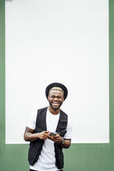 Lachender Mann mit Smartphone vor einer grün-weißen Wand - OCMF00983