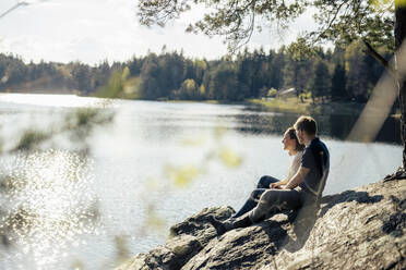 Affectionate couple sitting at the lakeside, Forstsee, Carinthia, Austria - DAWF01069