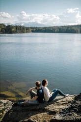 Happy couple sitting back to back at the lakeside, Forstsee, Carinthia, Austria - DAWF01080