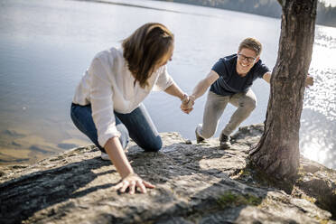 Glückliches Paar beim Klettern Hand in Hand am Seeufer, Forstsee, Kärnten, Österreich - DAWF01082