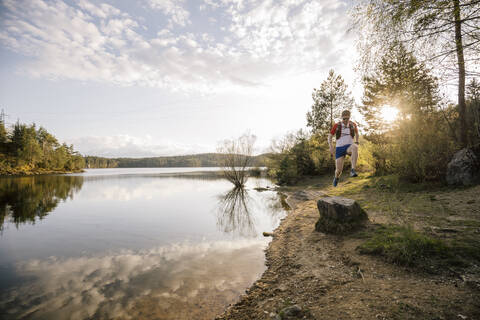 Mann läuft am See bei Sonnenuntergang, Forstsee, Kärnten, Österreich, lizenzfreies Stockfoto