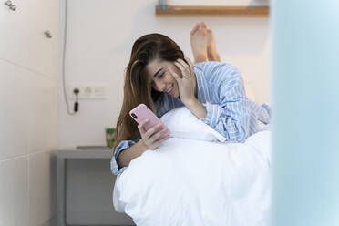 Young woman lying on bed and using smartphone in the morning - ERRF02532