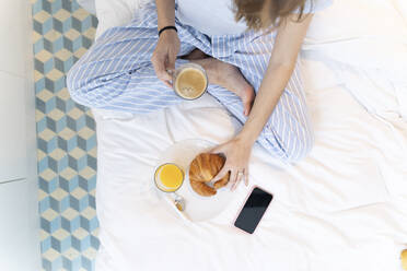 Junge Frau sitzt auf dem Bett und trinkt einen Kaffee - ERRF02535