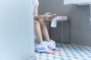 Young woman sitting on toilet and using smartphone - ERRF02554