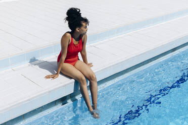 Junge Frau im roten Badeanzug entspannt sich am Pool - SODF00443