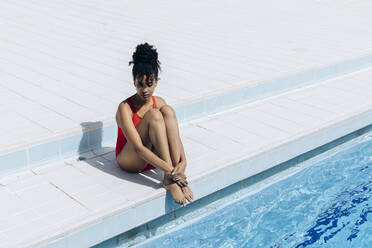 Nachdenkliche junge Frau im roten Badeanzug am Pool sitzend - SODF00444