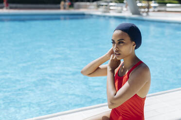 Porträt einer jungen Frau, die sich am Pool eine Badekappe aufsetzt - SODF00449