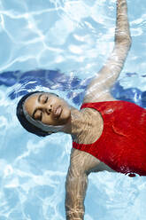 Portrait of young woman with eyes closed floating on water in swimming pool - SODF00465