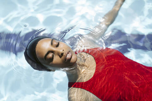 Porträt einer jungen Frau mit geschlossenen Augen, die auf dem Wasser im Schwimmbad schwimmt - SODF00466