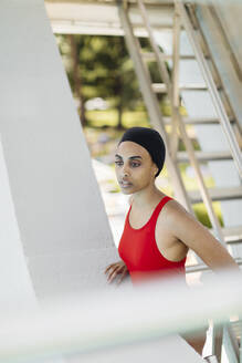 Porträt einer jungen Frau mit Badekappe und rotem Badeanzug auf der Treppe eines Highboards stehend - SODF00468