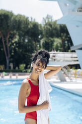 Porträt einer lächelnden jungen Frau im roten Badeanzug, die sich vor einem Pool abtrocknet - SODF00473