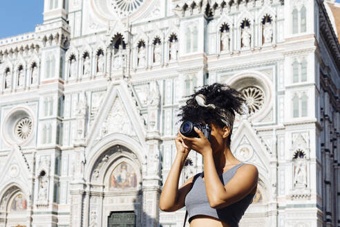 Young woman taking photo with camera in front of cathedral, Florence, Italy - SODF00487