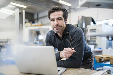 Portrait of businessman using laptop in a factory - DIGF09027