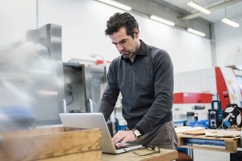 Geschäftsmann mit Laptop in einer Fabrik, lizenzfreies Stockfoto