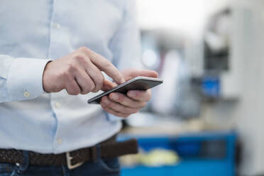 Close-up of businessman using cell phone in a factory - DIGF09075