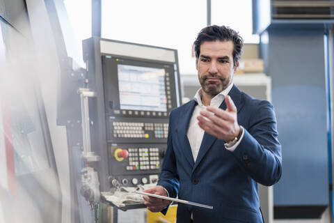 Geschäftsmann mit Tablet an einer Maschine in einer Fabrik, lizenzfreies Stockfoto