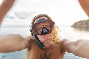 Junger Mann mit Schnorchel macht ein Gesicht am Strand - AFVF04979