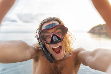 Junger Mann mit Schnorchel macht ein Gesicht am Strand - AFVF04980