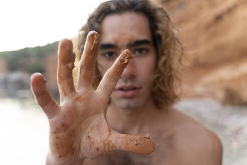 Junger Mann zeigt seine Hand mit Schlamm an einem Strand - AFVF04983