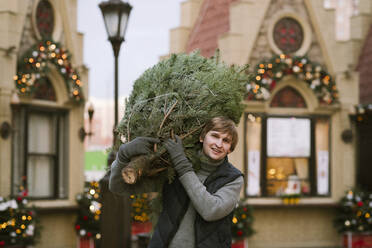 Lächelnder Mann mit Tannenbaum auf der Schulter - EYAF00794